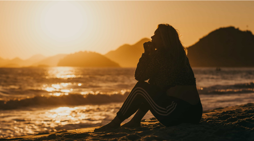 Woman sitting on beach looking at horizon