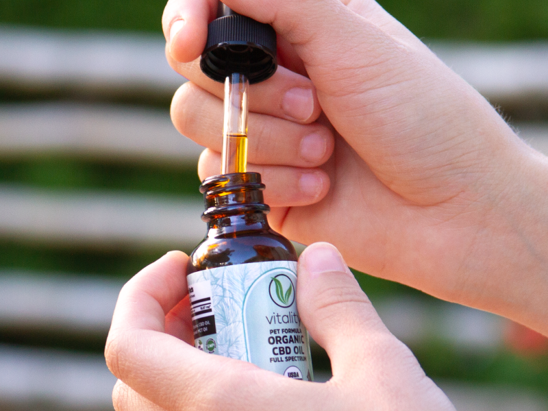 An open bottle of Vitality's CBD oil for pets with a full dropper coming out of it.