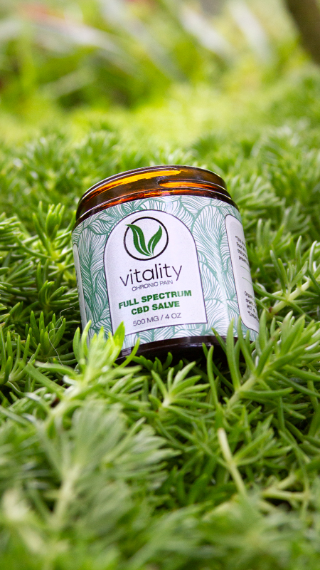 Open container of Vitality's CBD salve for chronic pain on the grass.