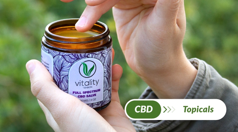 A hand getting some Vitality's CBD salve from an open container.