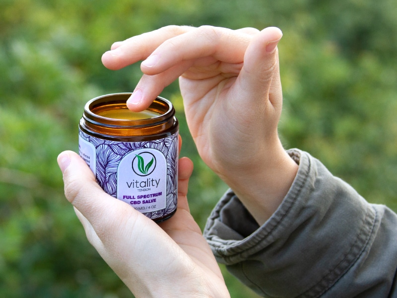 Hand holding an open container of Vitality's CBD salve.
