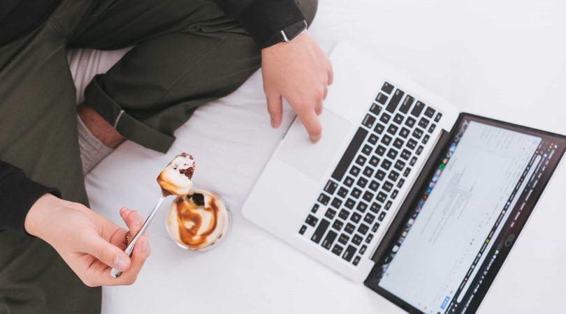 Person eating a healthy snack while working on a laptop.