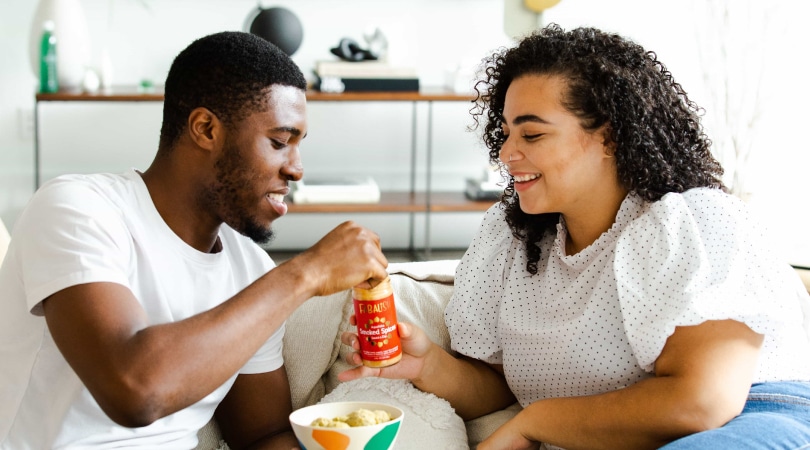 A woman and a man sitting on a couch and sharing a snack.