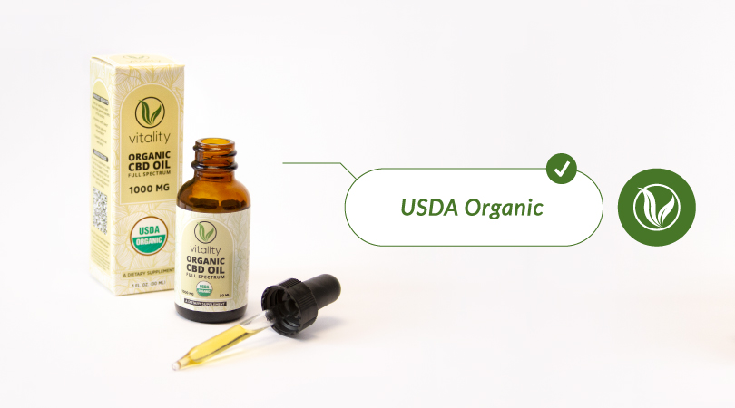 Open bottle of Vitality CBD oil with a full dropper of CBD on the side, with a text, next to it, that reads "USDA organic".