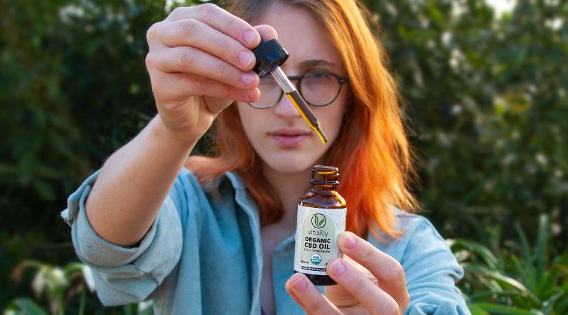 Woman holding a Vitality CBD oil bottle and dropper.