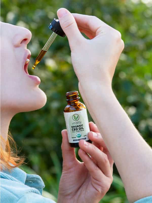 Woman taking Vitality CBD oil from a dropper.