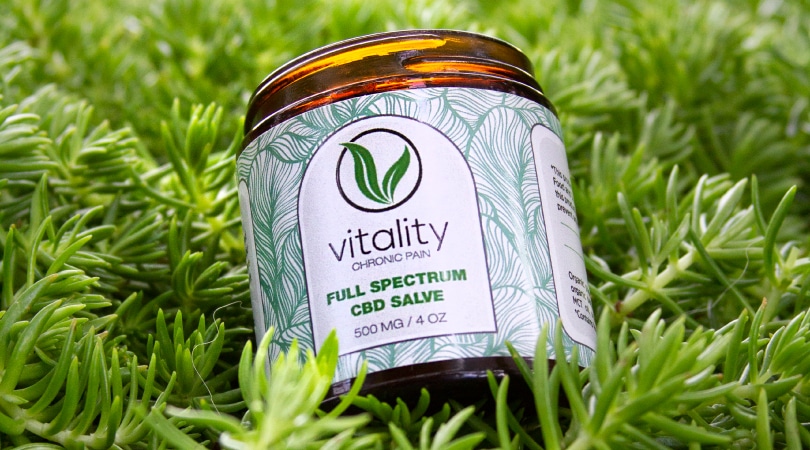 Open container of Vitality's CBD salve for chronic pain on the grass.