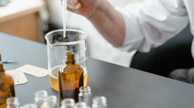 Hand holding a dropper above a beaker with CBD oil.