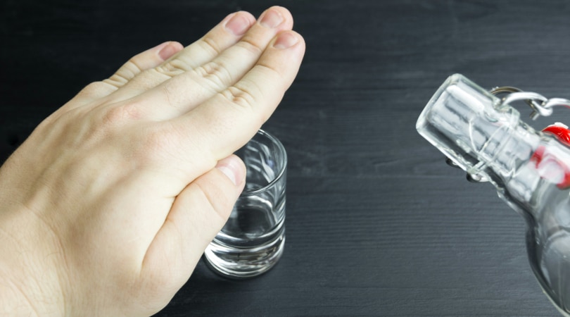 A hand covering a shot glass, blocking it, with an alcohol bottle next to it.