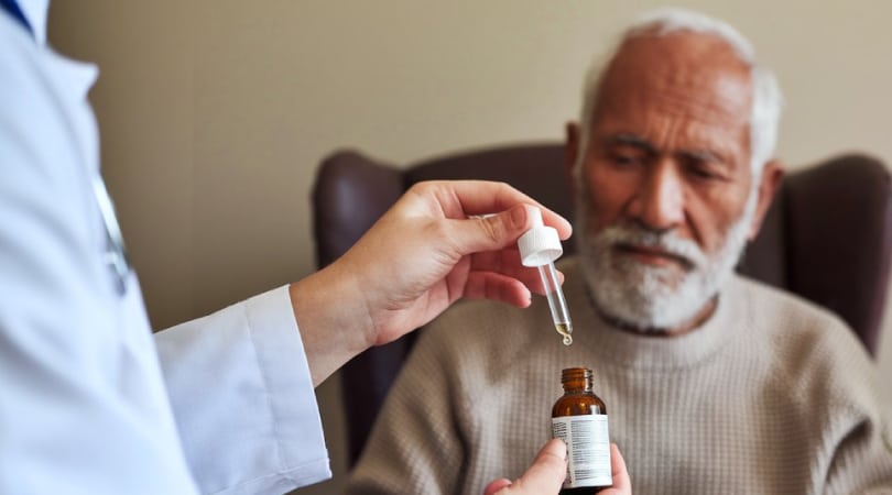 Doctor holding a CBD oil dropper and a patient on the background.