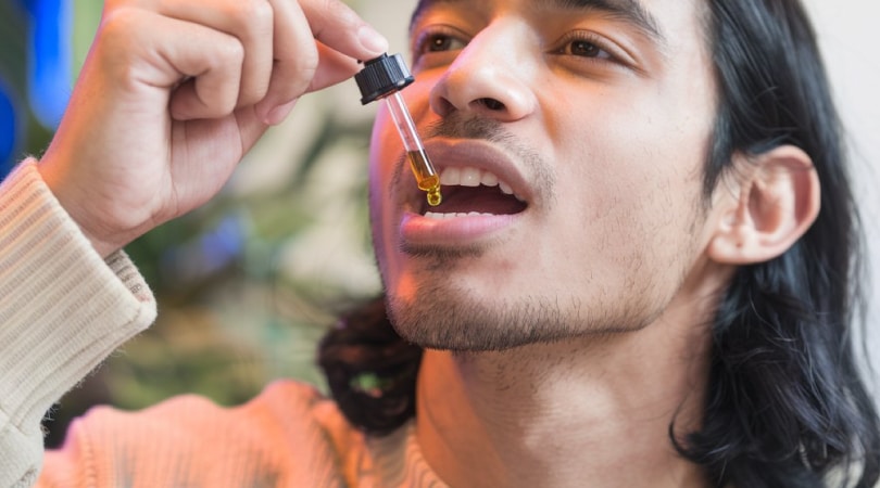 Man putting a dropper full of CBD oil in his mouth.