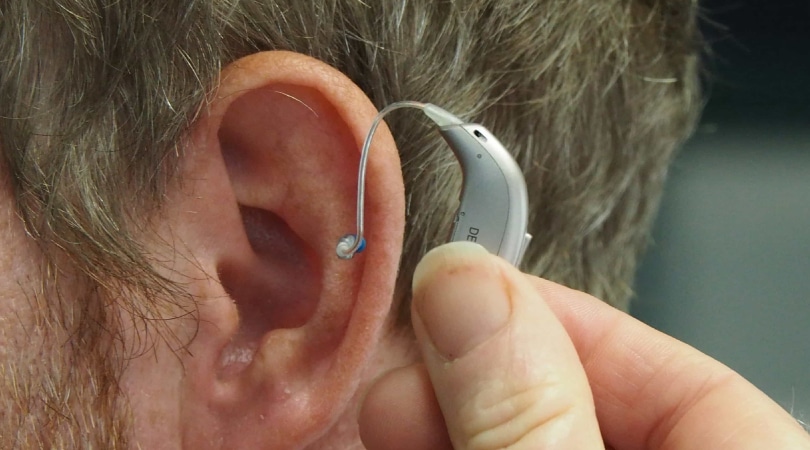 Man's ear with a hearing aid next to it.