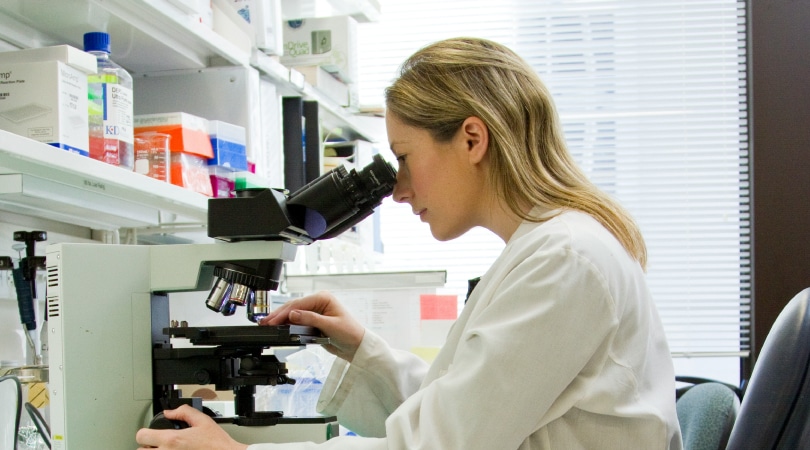 Female doctor looking through a microscope in a lab.