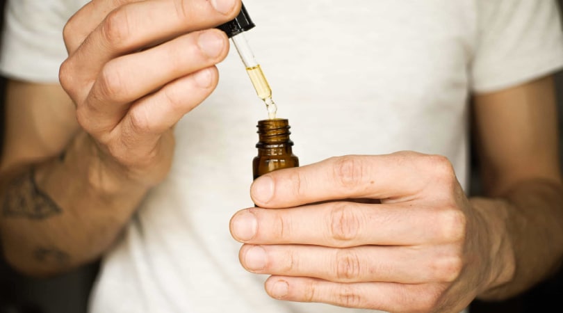 Man holding a bottle and a dropper full of CBD oil.